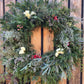 An 18-inch evergreen wreath with a mix of floral and berry elements, displayed on a wooden fence.