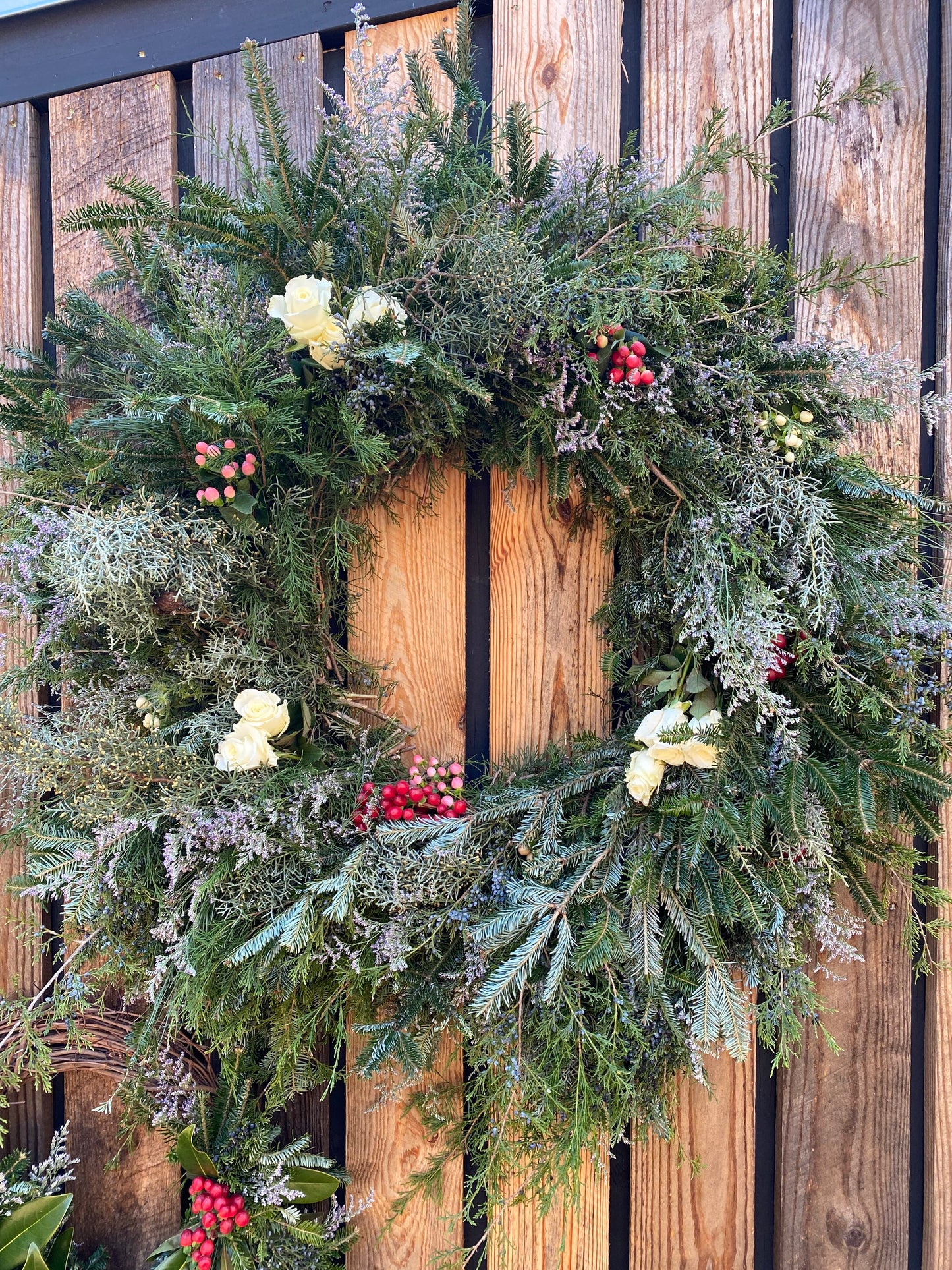 An 18-inch evergreen wreath with a mix of floral and berry elements, displayed on a wooden fence.
