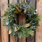 A 12-inch evergreen wreath with a mix of floral and berry elements, displayed on a wooden fence.