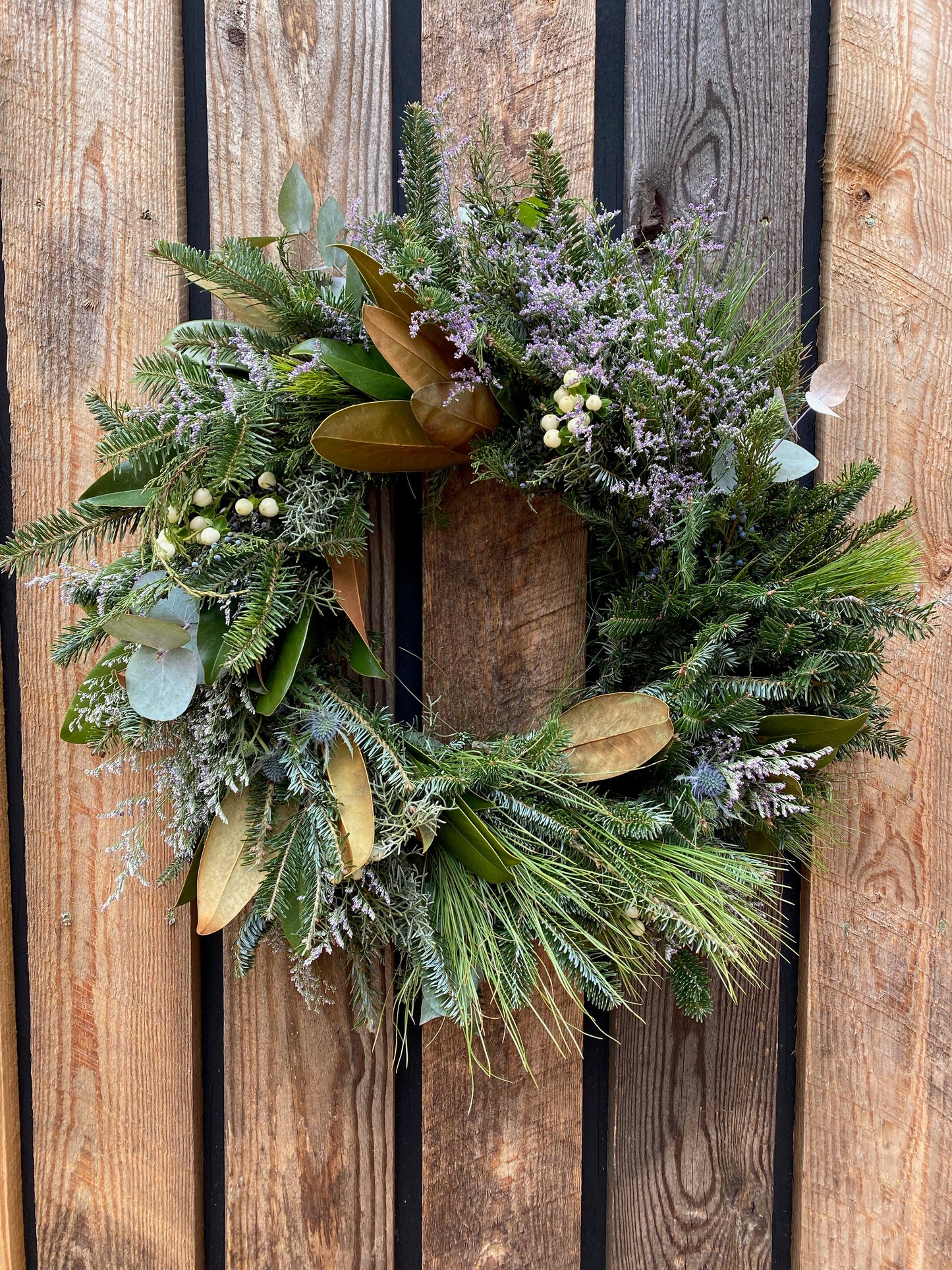 A 12-inch evergreen wreath with a mix of floral and berry elements, displayed on a wooden fence.